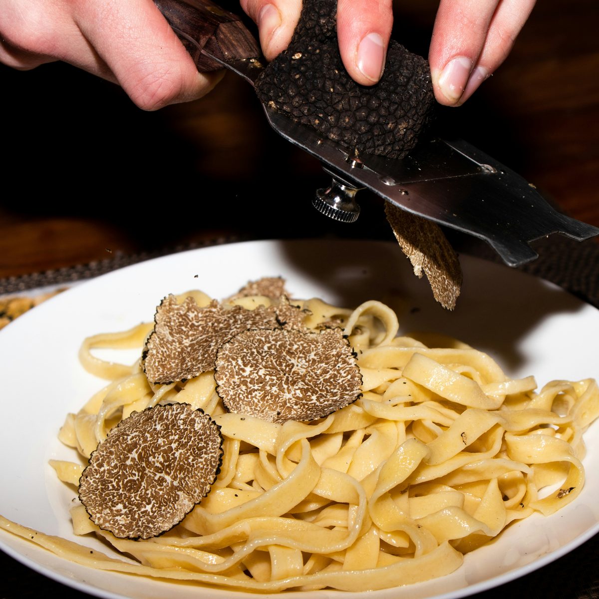 A nest of golden tagliatelle with shaved black truffle and parmesan in a cream bowl