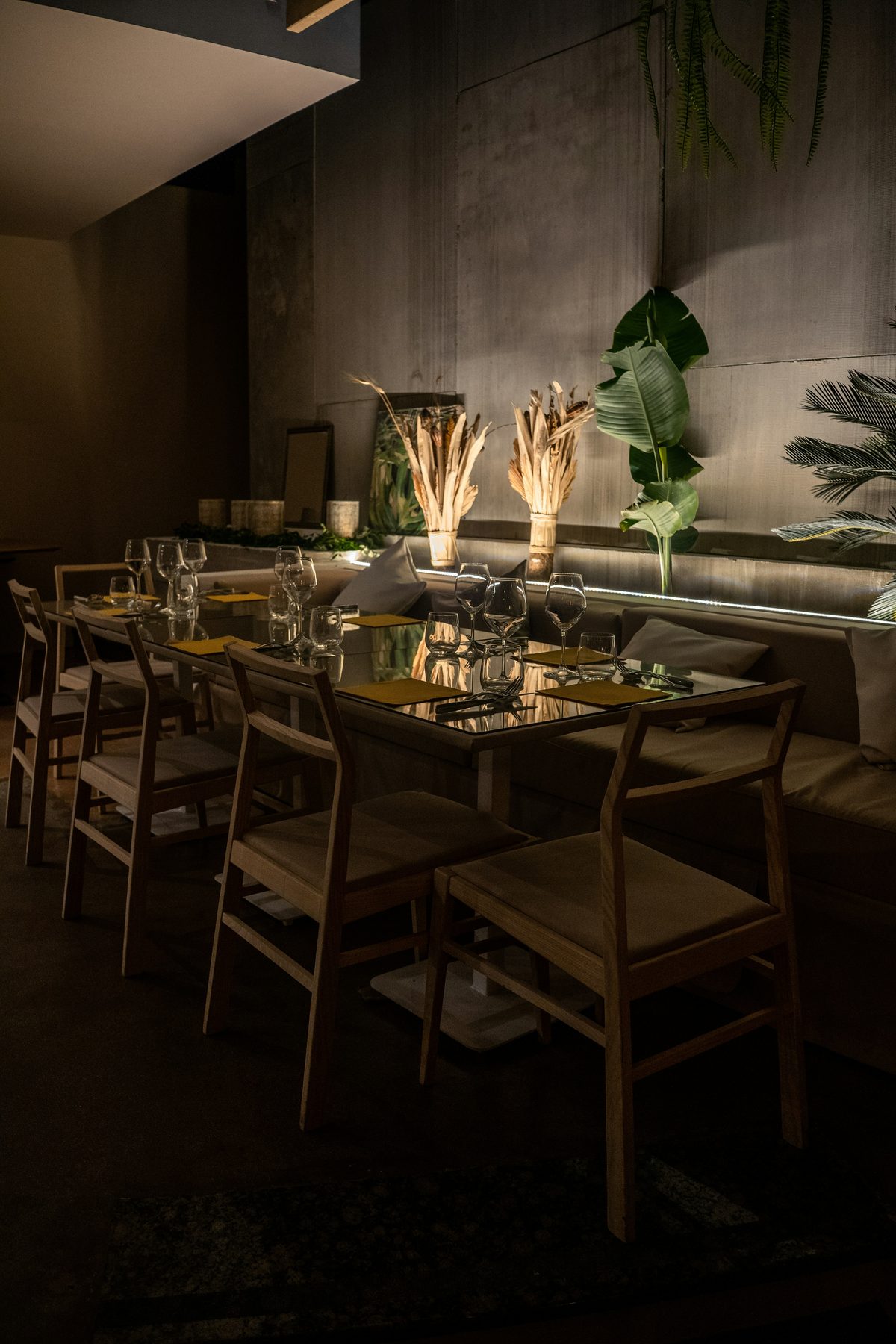 A long table set for dinner beneath warm light and plants